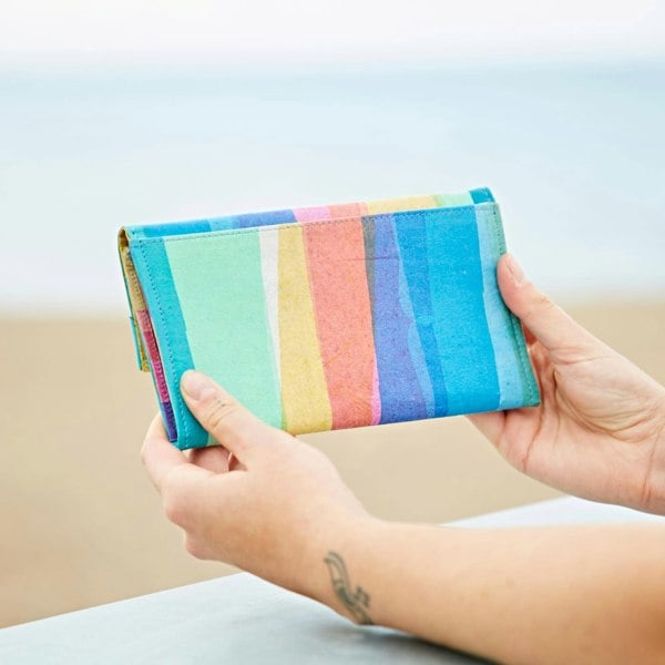 A woman holding up a Recycled Plastic Rainbow Clutch Purse on the beach.