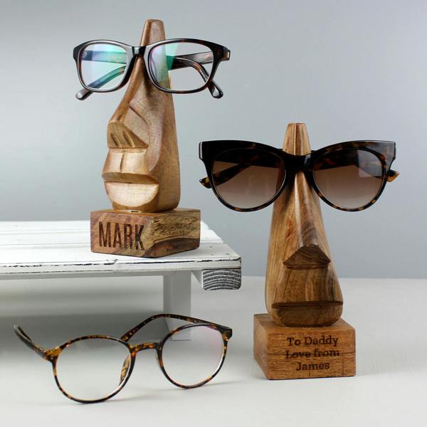 Two personalised nose-shaped acacia wood glasses holders displayed with reading glasses and sunglasses alongside an extra pair of frames.
