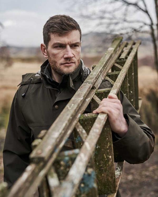 Man wearing Hoggs of Fife Green King II Waterproof Jacket whilst carrying a wooden ladder