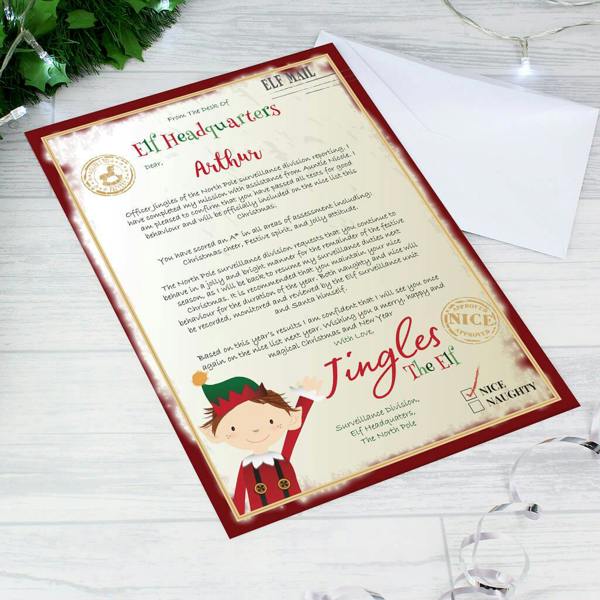 A colourful, official North Pole Elf Headquarters surveillance letter addressed to Arthur from Jingles the Elf, showing a white presentation envelope on a wooden table.