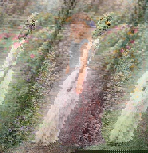 Young girl in a white top and pink tulle skirt standing in a garden with cherry blossoms.