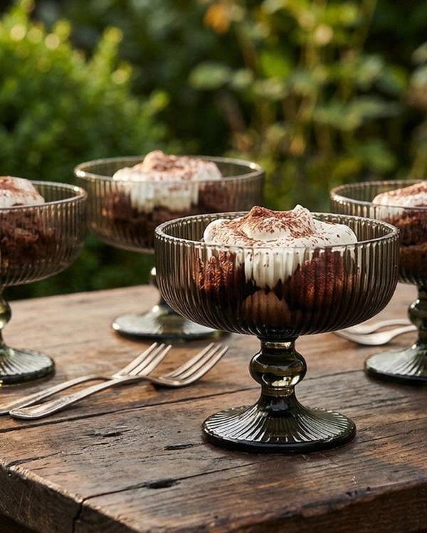 Four dark grey glass dessert bowls on a wooden surface with decorative elements.