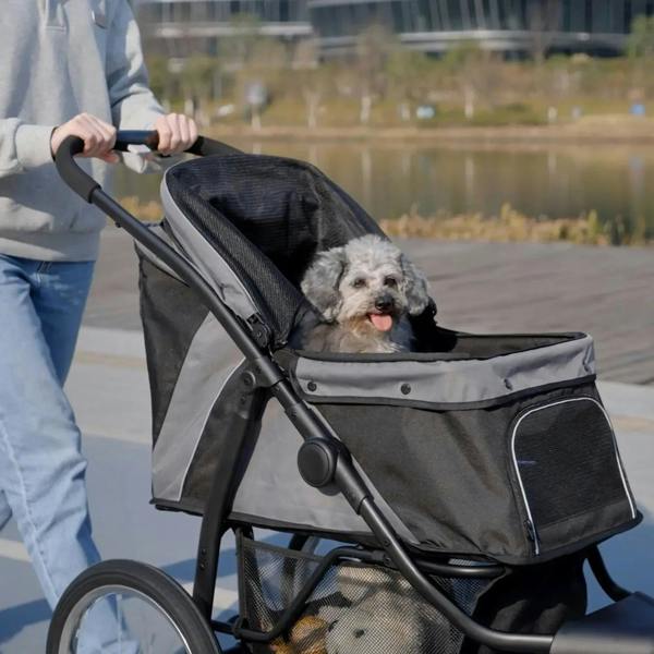 Grey three-wheel pet stroller with open front mesh panel and dog sitting inside