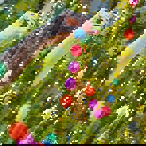A person is holding a Handmade Multicoloured Felt Ball Garland on a christmas tree.