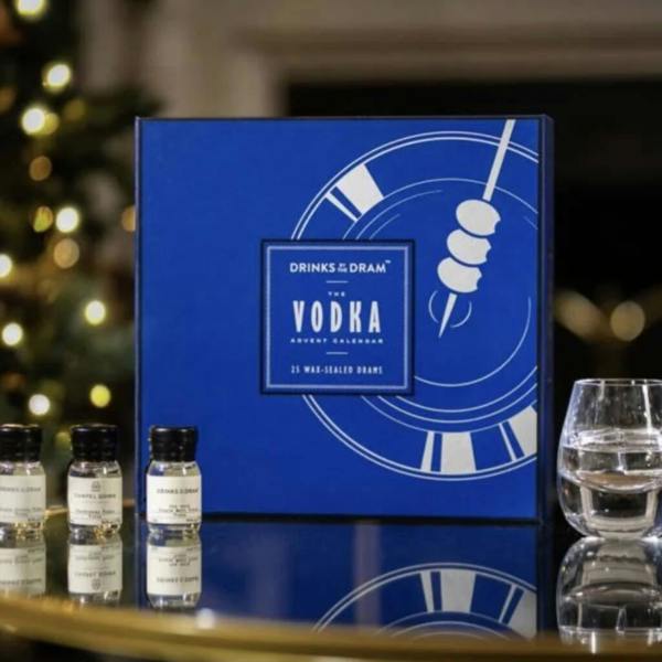 A royal blue Drinks by the Dram Vodka Advent Calendar box resting on a glass table next to three miniature wax-sealed bottles.