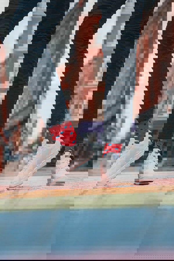 Person wearing white sneakers and red socks with black polka dots on a city street.