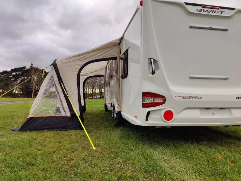 The OLPRO View Lite Breeze 390 Caravan Awning pictured in a Caravan site attached to a caravan with the side doors open.