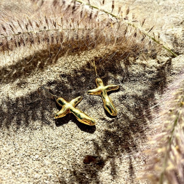 Gold vermeil cross drop earrings photographed on sand.