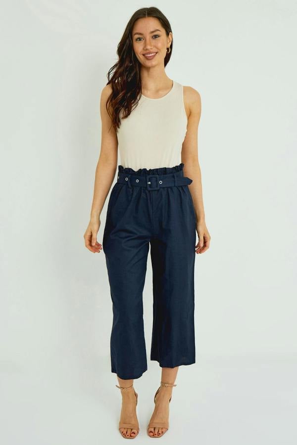 Woman wearing a white sleeveless top and navy wide-leg pants on a white background