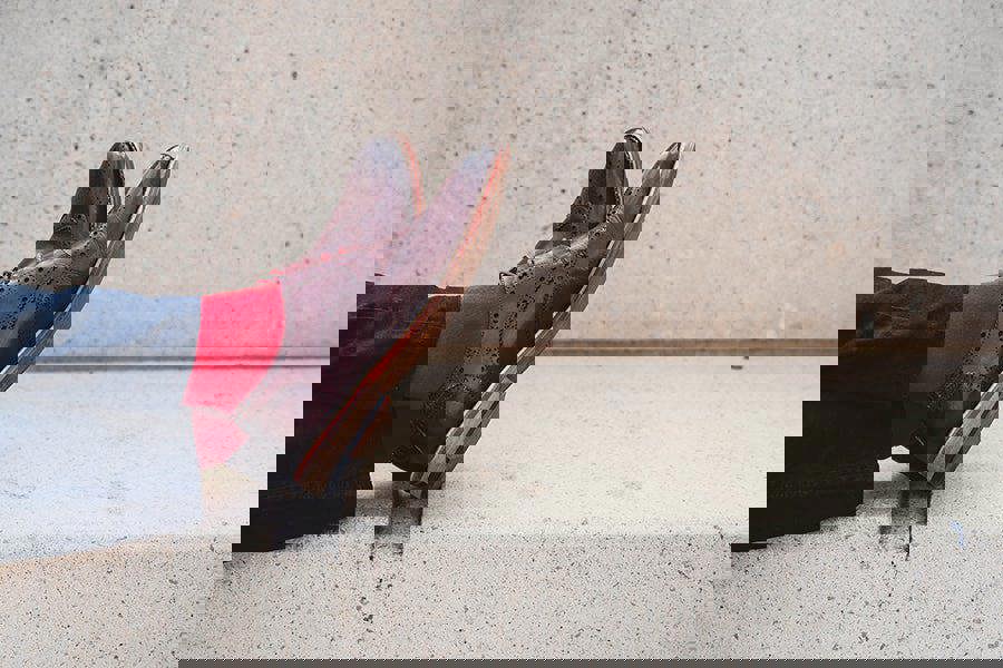 Brown dress shoes with red socks and a red shirt against a concrete wall.