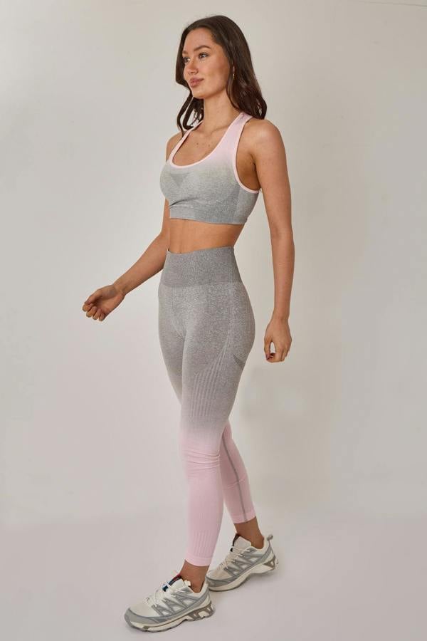 Woman wearing a gray sports bra and leggings with pink accents on a plain background