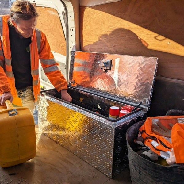 Extra large aluminium tool box with diamond plate texture, open to reveal tools inside, placed in a work van with safety gear nearby