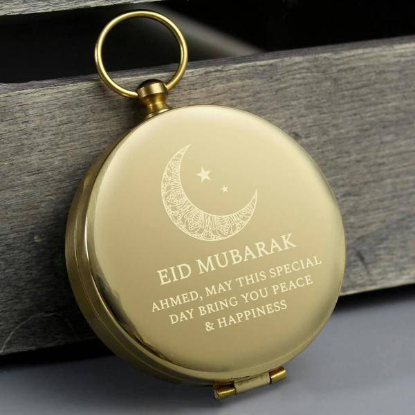 A brushed brass pocket compass engraved with a crescent moon, 'EID MUBARAK', and a custom message for Ahmed.