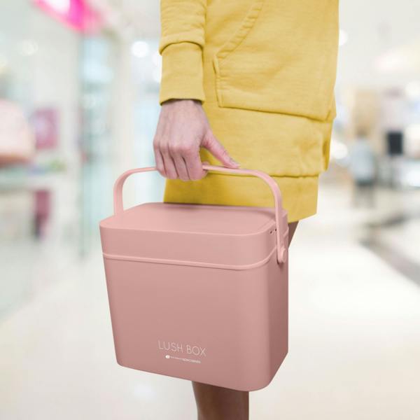 A person in a yellow outfit holds the Rio Lush Box Vanity Case - Large by its handle while standing indoors, possibly in a mall—ideal for stylish, on-the-go beauty storage.