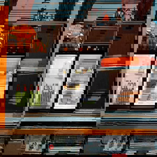 Compact 3-way absorption fridge with a sleek black exterior, showcasing drinks and food storage inside, set in a cozy van interior