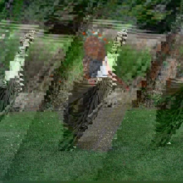 Young girl in a long green dress with a flower crown standing on grass.