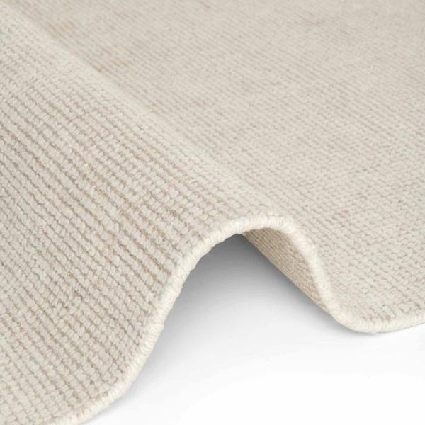 Close-up of a textured beige rug corner on a light gray background