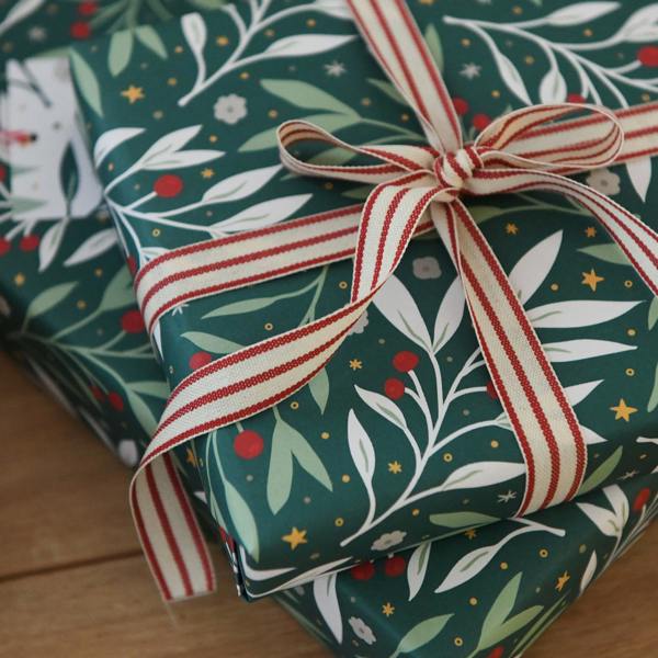 Green festive foliage Christmas wrapping paper tied with a red and cream striped ribbon alongside a matching gift tag.