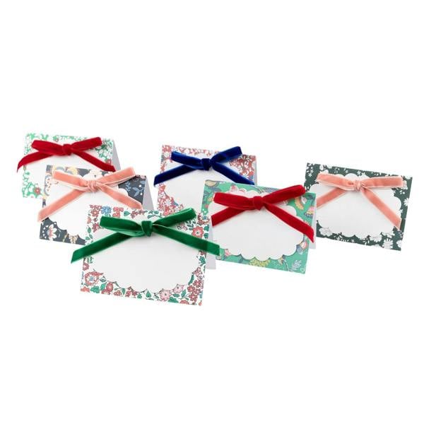 A set of six luxury floral Christmas place cards featuring colourful heritage patterns, scalloped name tags, and rich velvet bows in red, blue, green, and pink.