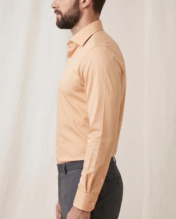 Man wearing a beige dress shirt and dark pants against a plain background