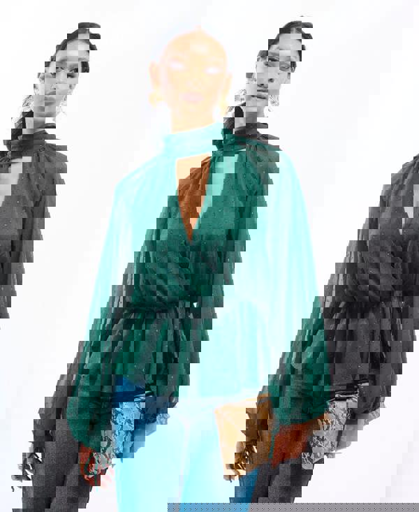 Woman wearing a green blouse with sheer sleeves and cut-out design, holding a snake skin clutch.