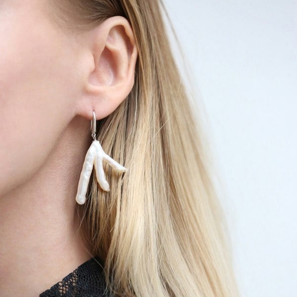 Close up of an ear with unique and irregular baroque pearl earrings.