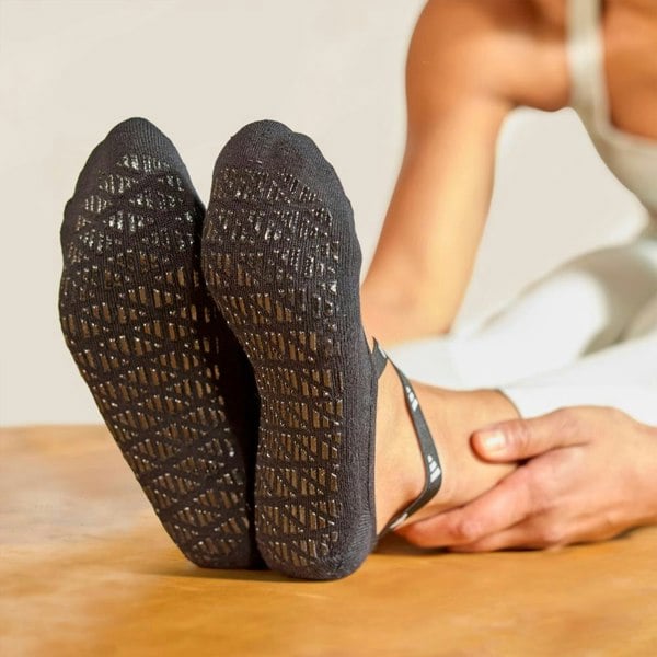 Person wearing black adidas textured yoga socks sitting on a wooden surface.