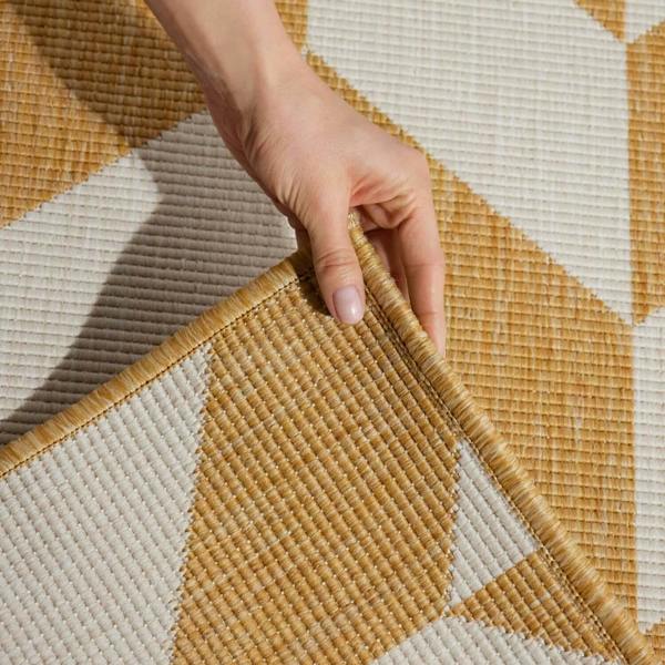 Hand touching a geometric-patterned woven mat with earthy tones.