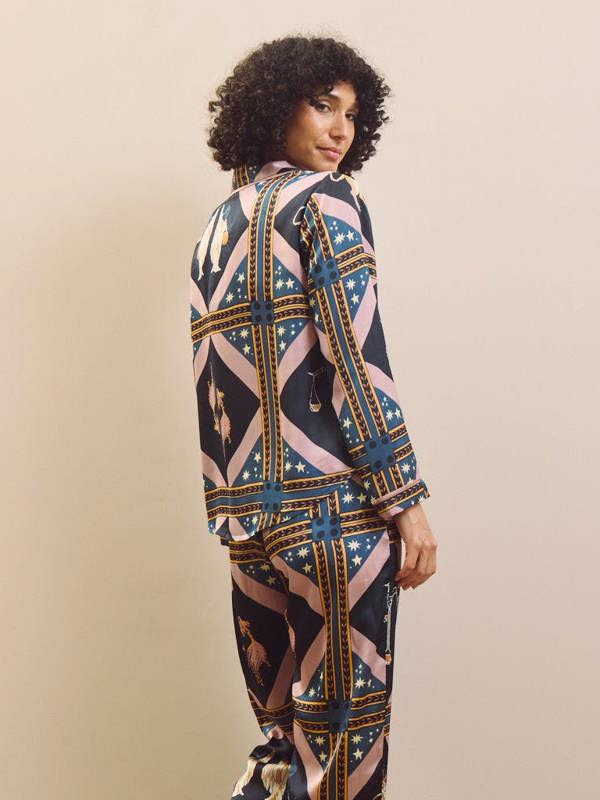 Woman wearing a celestial patterned satin pyjamas standing against a plain wall.