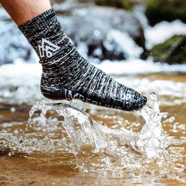 A person splashing their foot into a shallow rocky river stream, wearing a black and white speckled mid-calf waterproof outdoor sock.