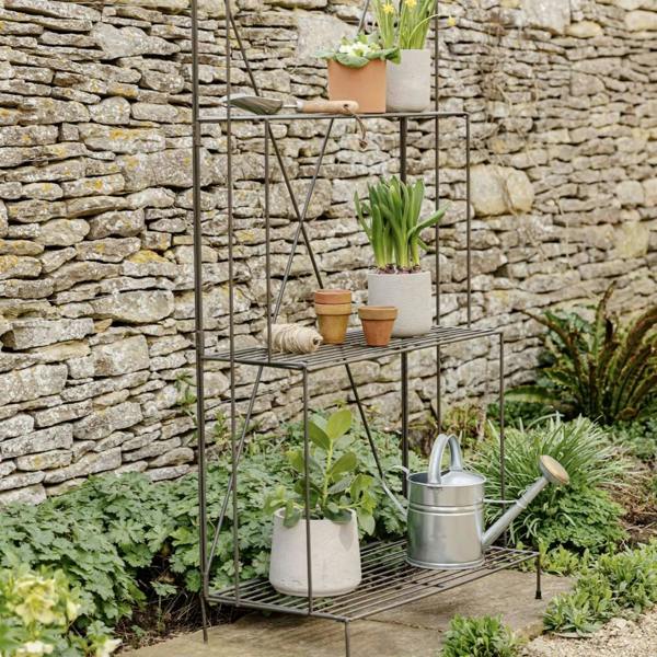 A tall charcoal grey industrial steel three-tier plant stand holding various green potted houseplants, shown against a plain backdrop.