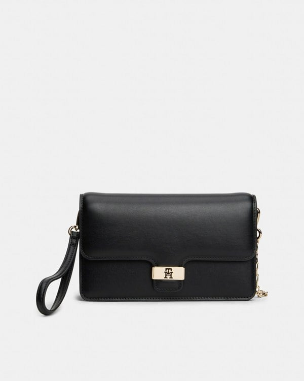 Black Tommy Hilfiger clutch bag with a gold logo clasp on a light grey background