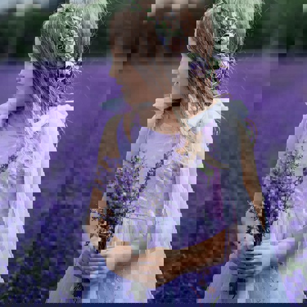Young girl in a lavender field wearing a floral headband and holding lavender flowers.