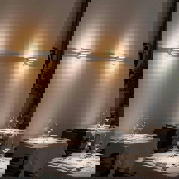 White indoor LED sconce light above tables in a restaurant on a pale grey wall
