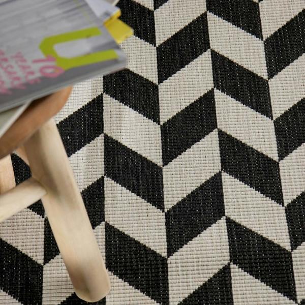 Close-up of a black and white geometric patterned rug with a wooden stool and colorful book.