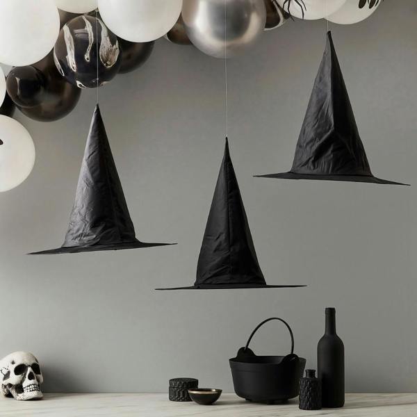 Three black witch hats hanging from clear twine appearing to float in mid air above a Halloween table display