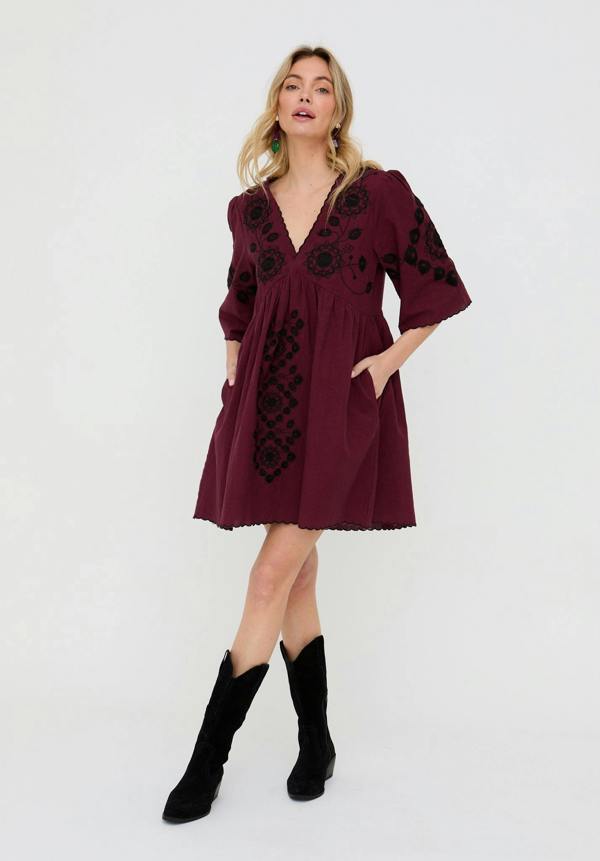 Woman wearing a burgundy dress with black floral embroidery on a white background