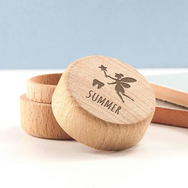 A small round wooden keepsake box with a lid leaning against it, engraved with a tooth fairy icon and the custom name Summer.