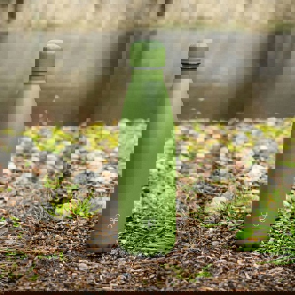 A Forest Green water bottle sits at the edge of a pond in a park.