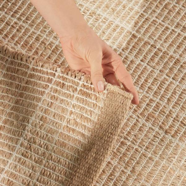 Hand holding a corner of a textured beige rug