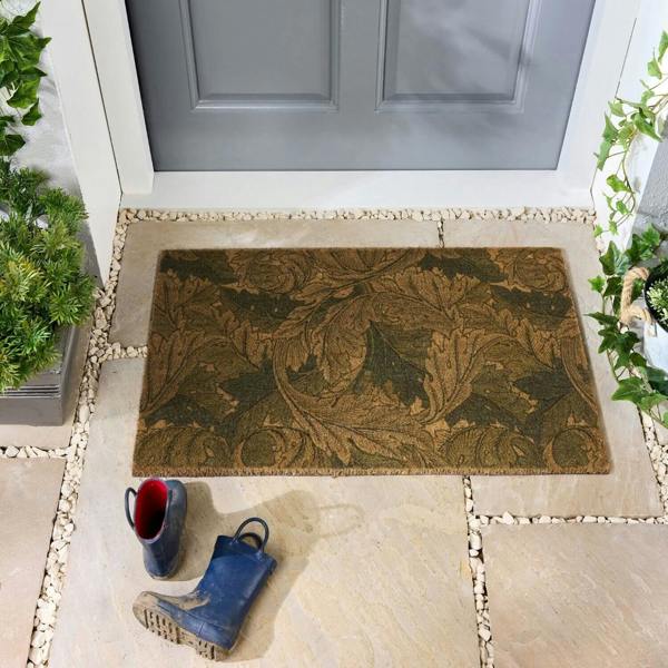 Decorative doormat with leaf pattern on a stone patio in front of a gray door.
