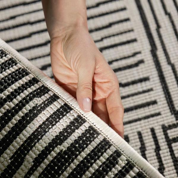Hand holding a corner of a black and white patterned rug