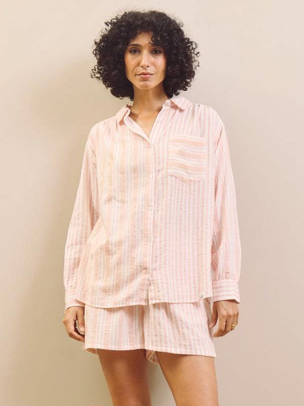 Woman wearing a light pink pyjama set against a plain background