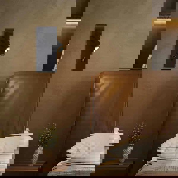 black dimmable reading light mounted on a textured wall next to the bed