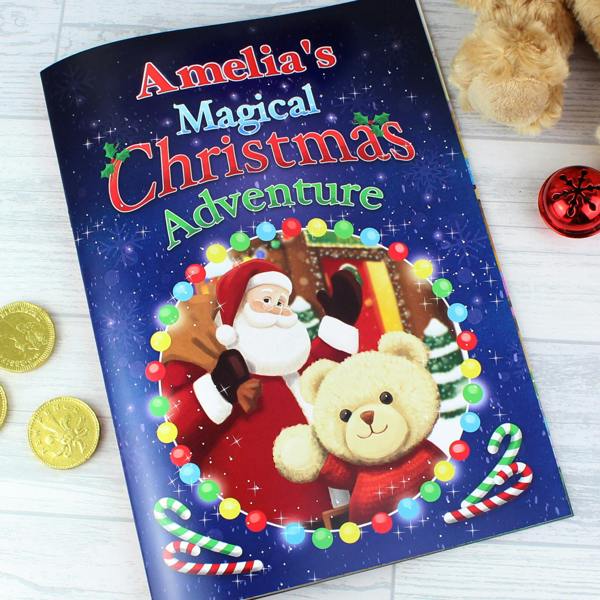 A personalised children's Christmas story book titled Amelia's Magical Christmas Adventure, showing Santa and a teddy bear encircled by fairy lights on a wooden surface.