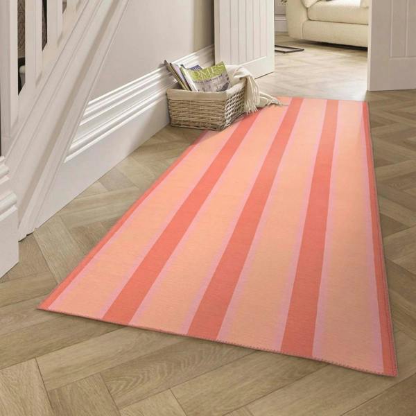 Striped pink and orange rug on a wooden floor with a white staircase in the background.