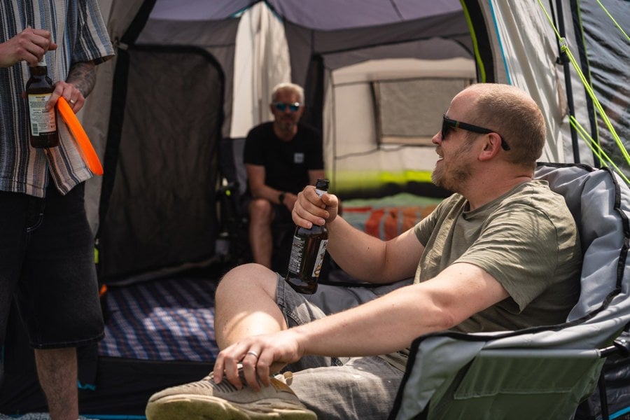 A group of males relaxing in camping furniture outside of the Hive 6 Berth Poled Tent by OLPRO