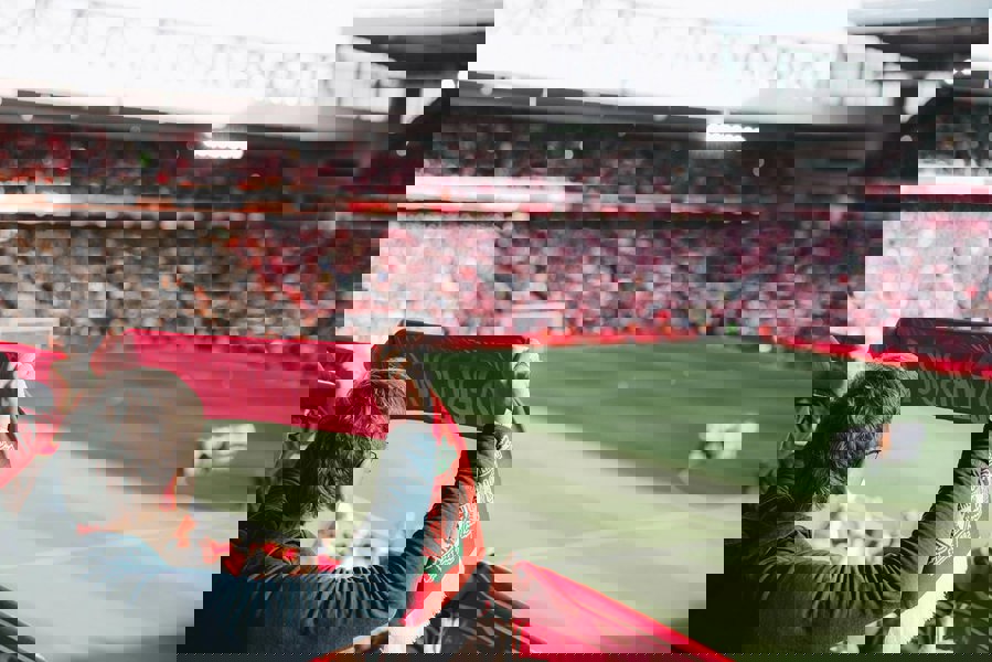 Person holding a red and white scarf in a football stadium with the football pitch in the background. Ruffnek snoods the offside rule.