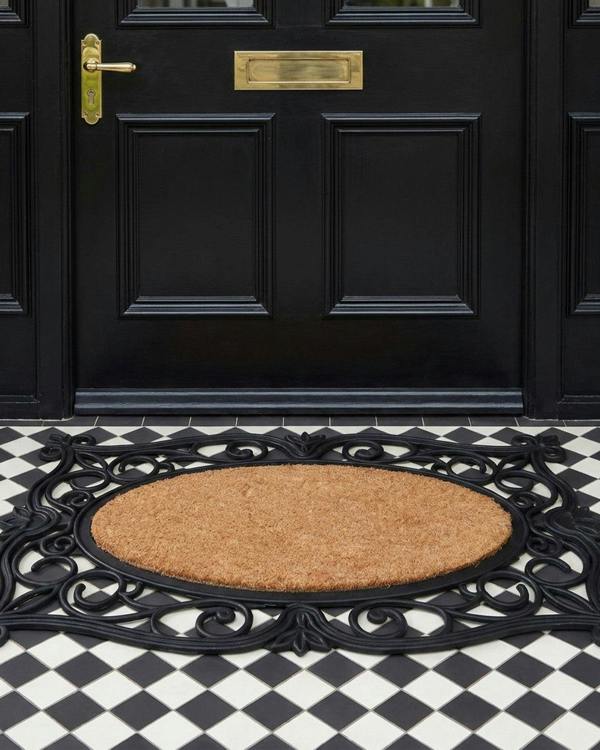 Decorative doormat with intricate design in front of a black door on a checkered floor.