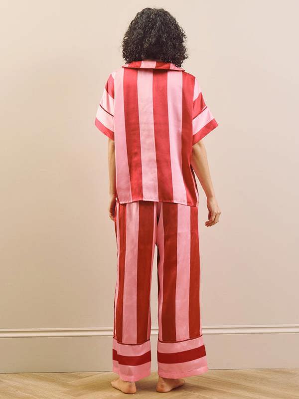 Model wearing a pink striped long pyjama set standing against a plain wall. Back detail.